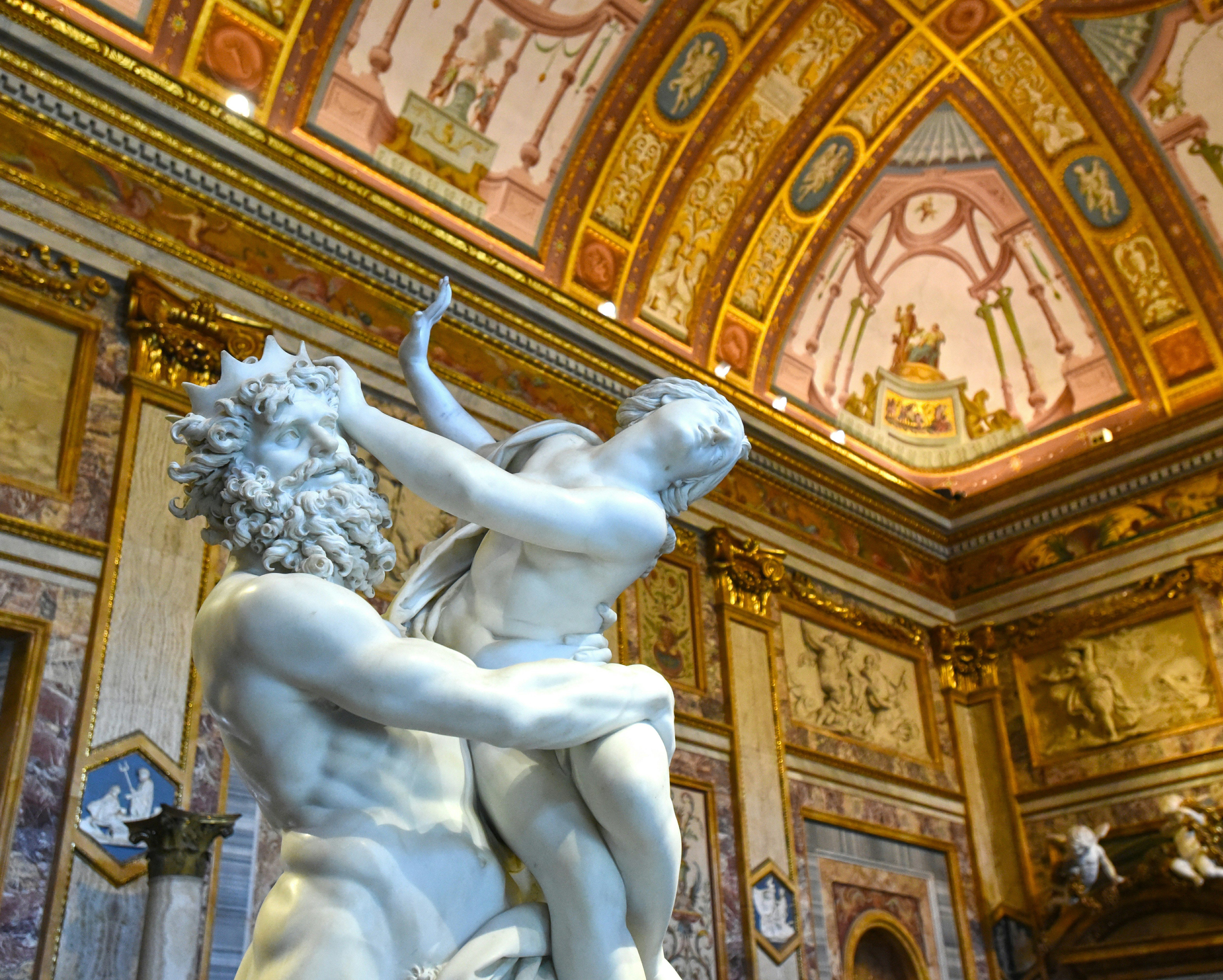 White marble sculpture of two figures embracing in a richly gilded, ornate room with painted ceilings and gold-trimmed panels